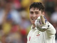 Cricketer smiling and pointing with a glove.