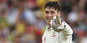 Cricketer smiling and pointing with a glove.