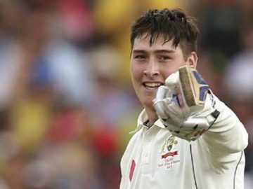 Cricketer smiling and pointing with a glove.