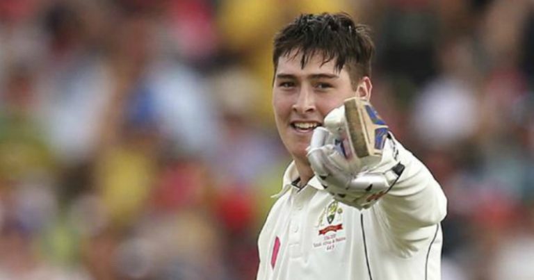 Cricketer smiling and pointing with a glove.