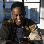 Man smiling while looking at his phone indoors.