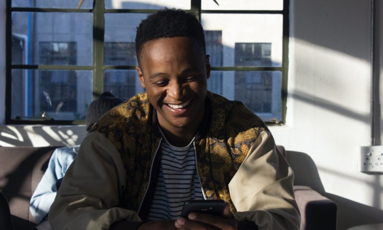 Man smiling while looking at his phone indoors.