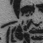 Black and white stencil art of man's face on wall.