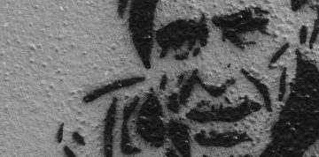 Black and white stencil art of man's face on wall.