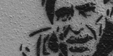 Black and white stencil art of man's face on wall.