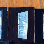 Three paintings of blue doors on wooden floor.