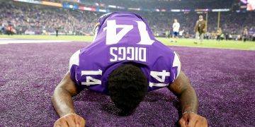 American football player kneeling on field, celebrating.