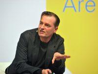 Person speaking at a conference, yellow background.