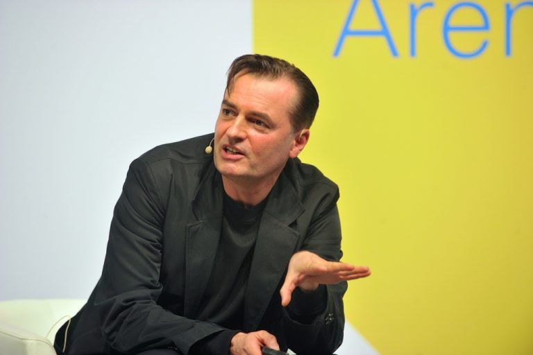 Person speaking at a conference, yellow background.