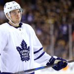 Hockey player in Toronto Maple Leafs jersey, holding stick.